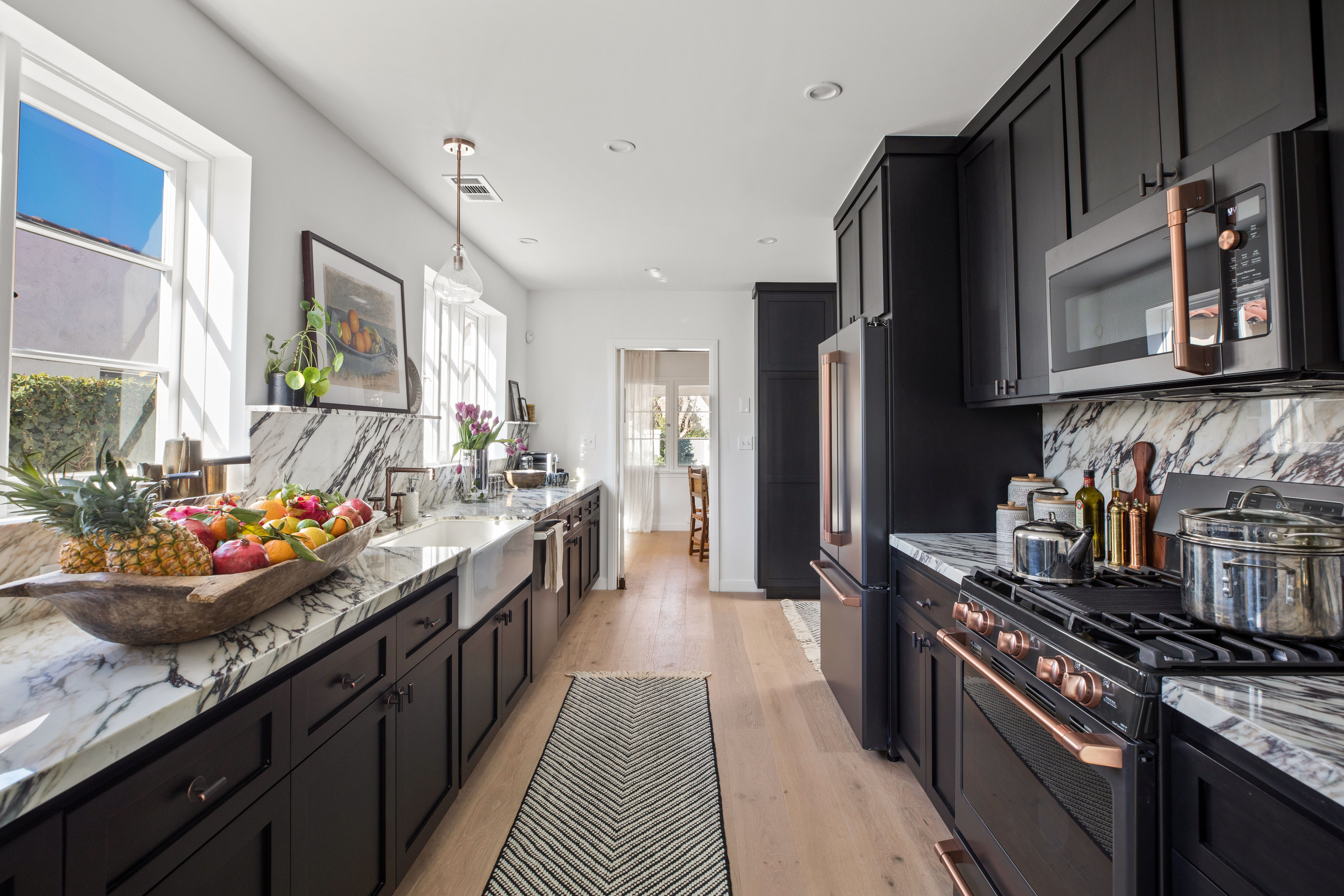 A galley kitchen with dark cabinets, a wide passageway in the centre and marble worktops