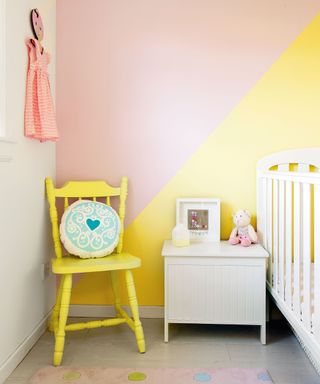 Child's nursery, bedroom with white cot and bedside table and yellow wooden chair, diagonal painted wall in yellow and pink