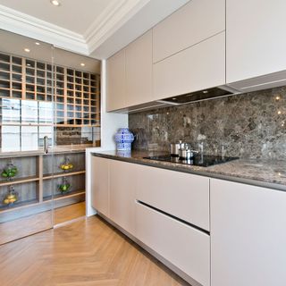 Stunning kitchen with natural stone surface and white cupboards next to walk-in wine fridge with 2 glass doors
