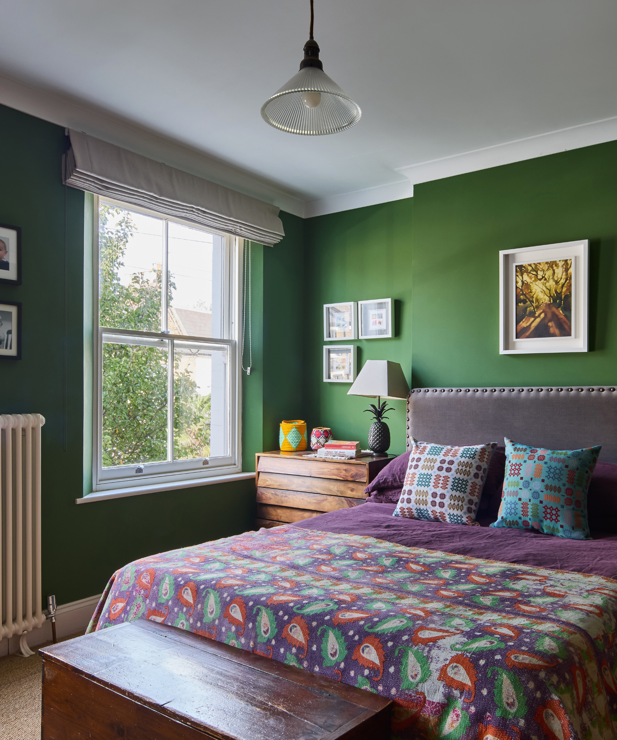 Bedroom with green walls, purple bedding and a window the left hand side of bed