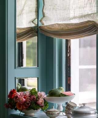 sheer linen roman blind in a blue painted window reveal with vintage trinkets