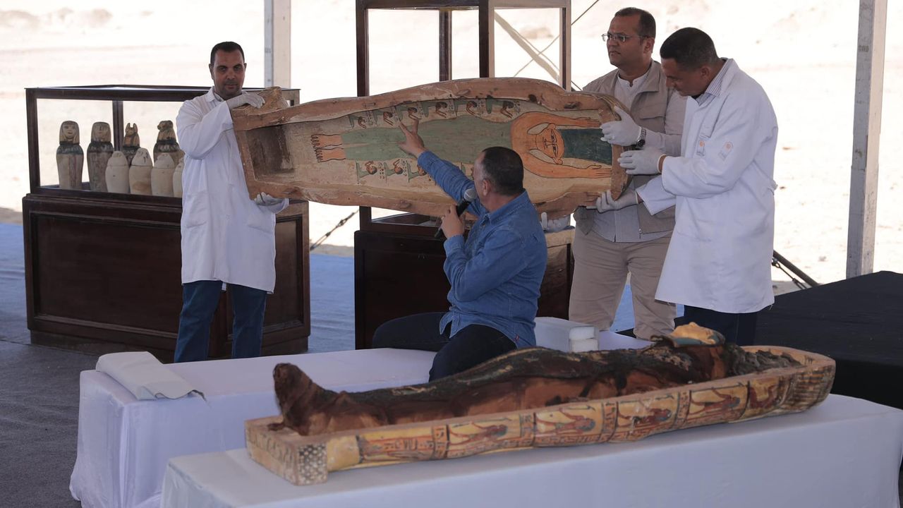 A coffin is opened at a press conference, revealing a mummy.