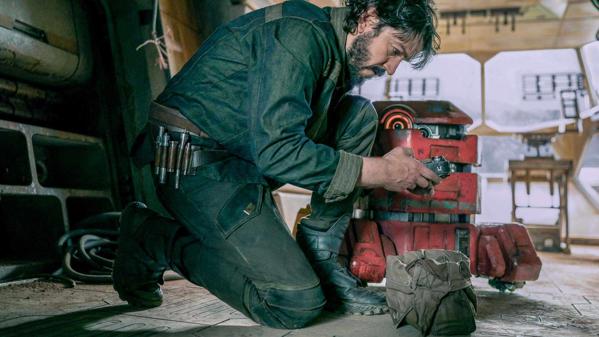 (L to R) Cassian Andor (Diego Luna) kneels examining something while B2EMO (Dave Chapman) stands to his left in Andor