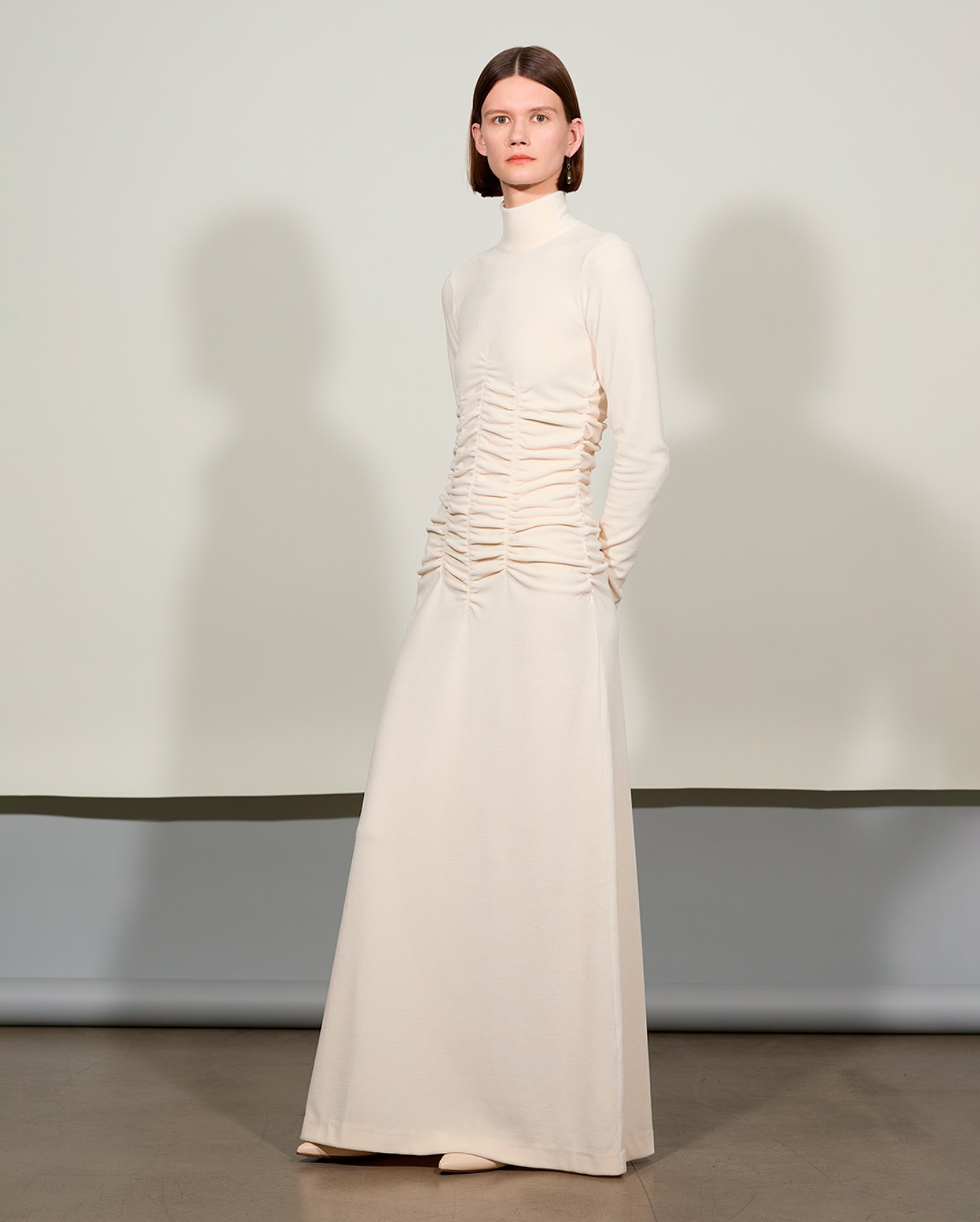 A woman wears a long white maxi dress with ruched details.