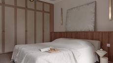 A bedroom with a scandi design and on top of the bed is an open book and a wooden board and a glass with a beverage inside