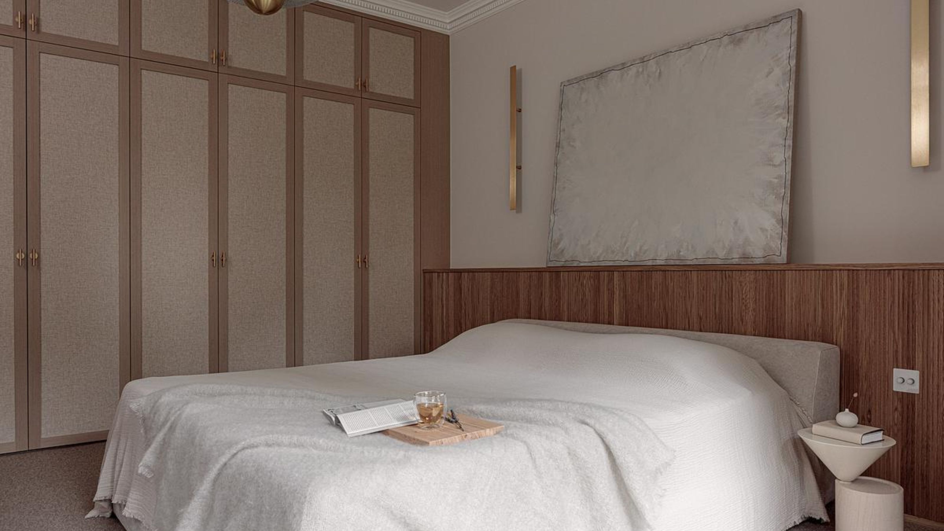A bedroom with a scandi design and on top of the bed is an open book and a wooden board and a glass with a beverage inside 