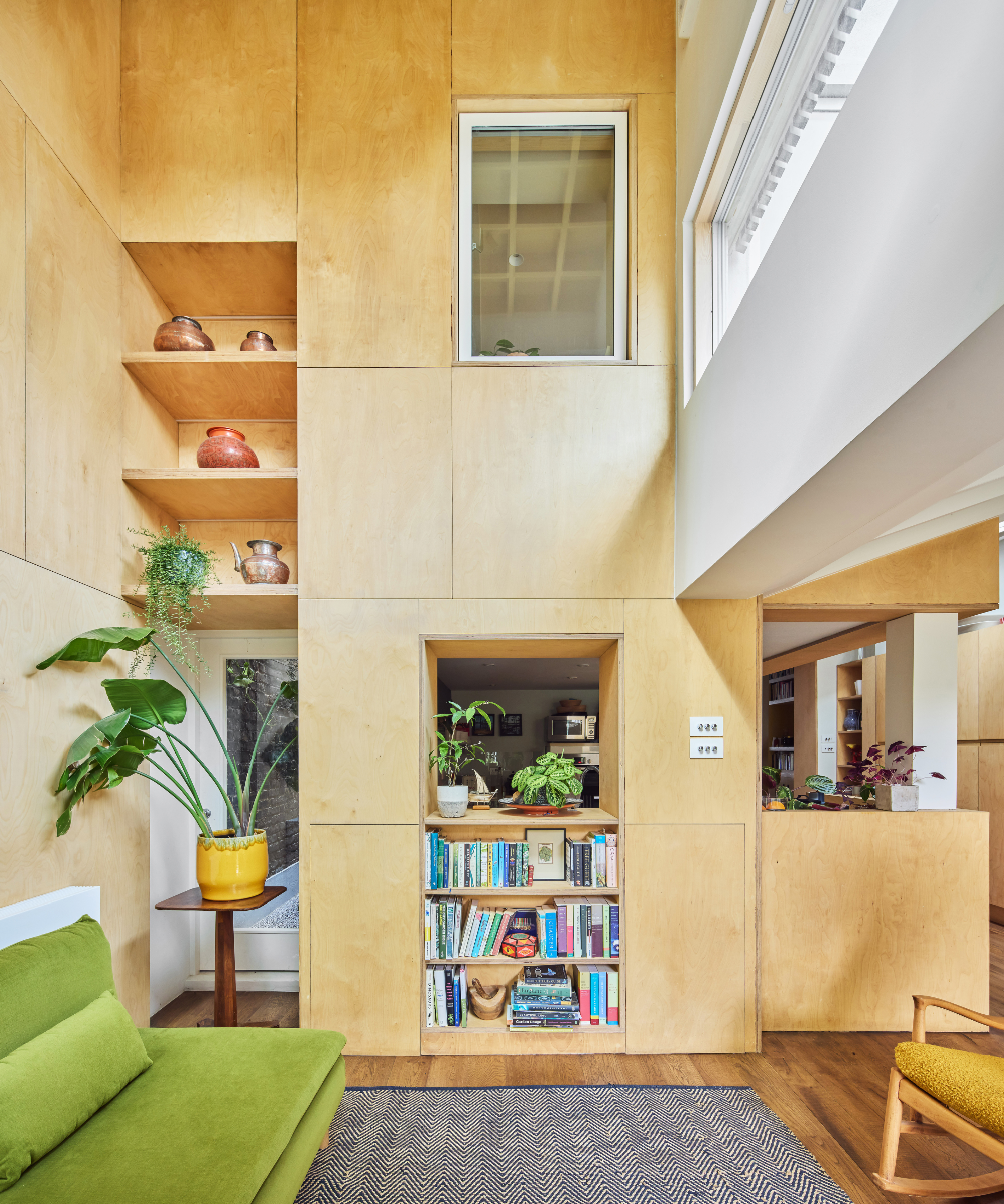 Living area with birch playwood sheets on the walls, a green sofa, and built in bookcase and shelving