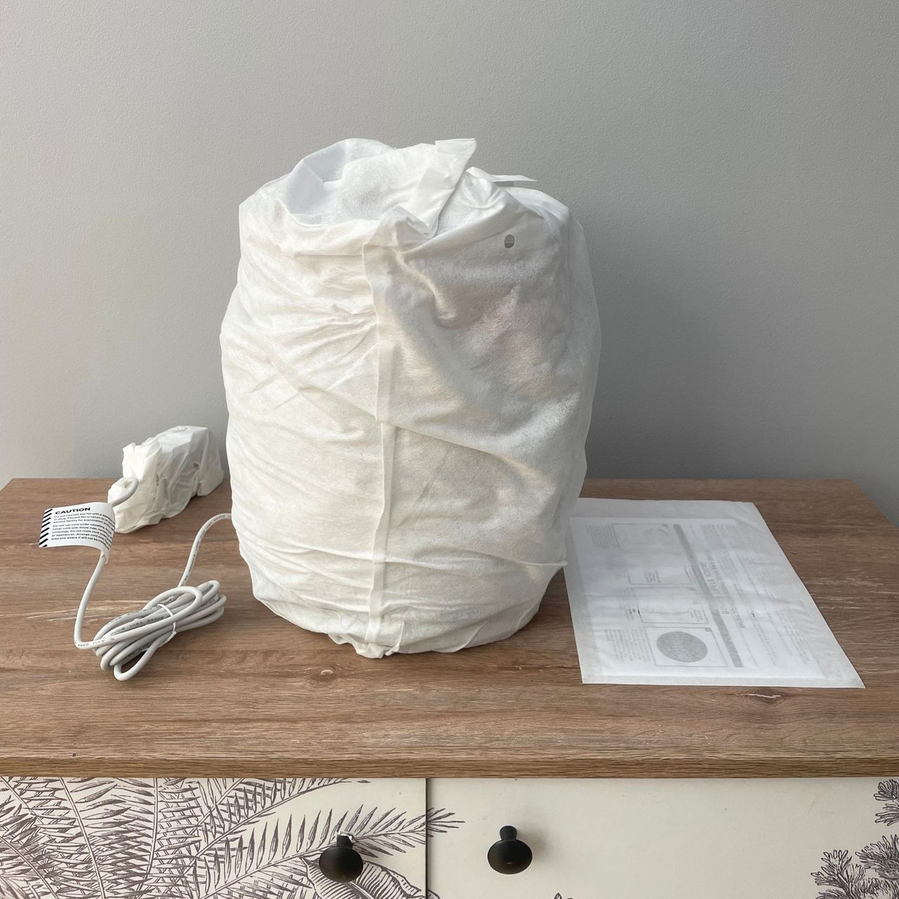 Shark BreatheClear Compact Air Purifier with NeverChange6 wrapped in packaging on a wooden unit in front of a grey wall