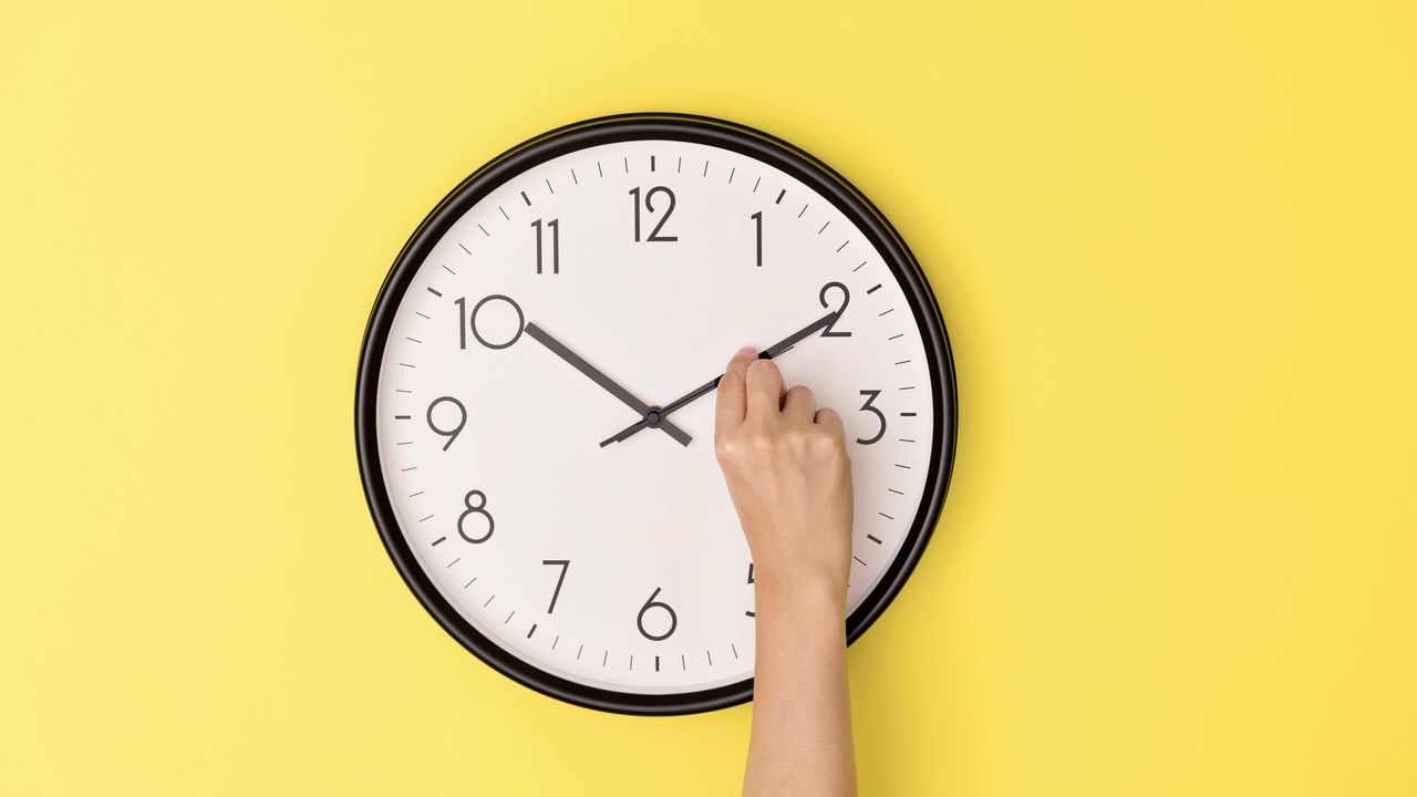 Somebody adjusting the minute hand on a clock hanging on a yellow wall