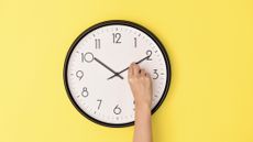Somebody adjusting the minute hand on a clock hanging on a yellow wall