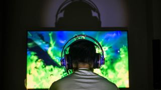 Young man wearing headphones watches an explosion on a computer monitor intently 