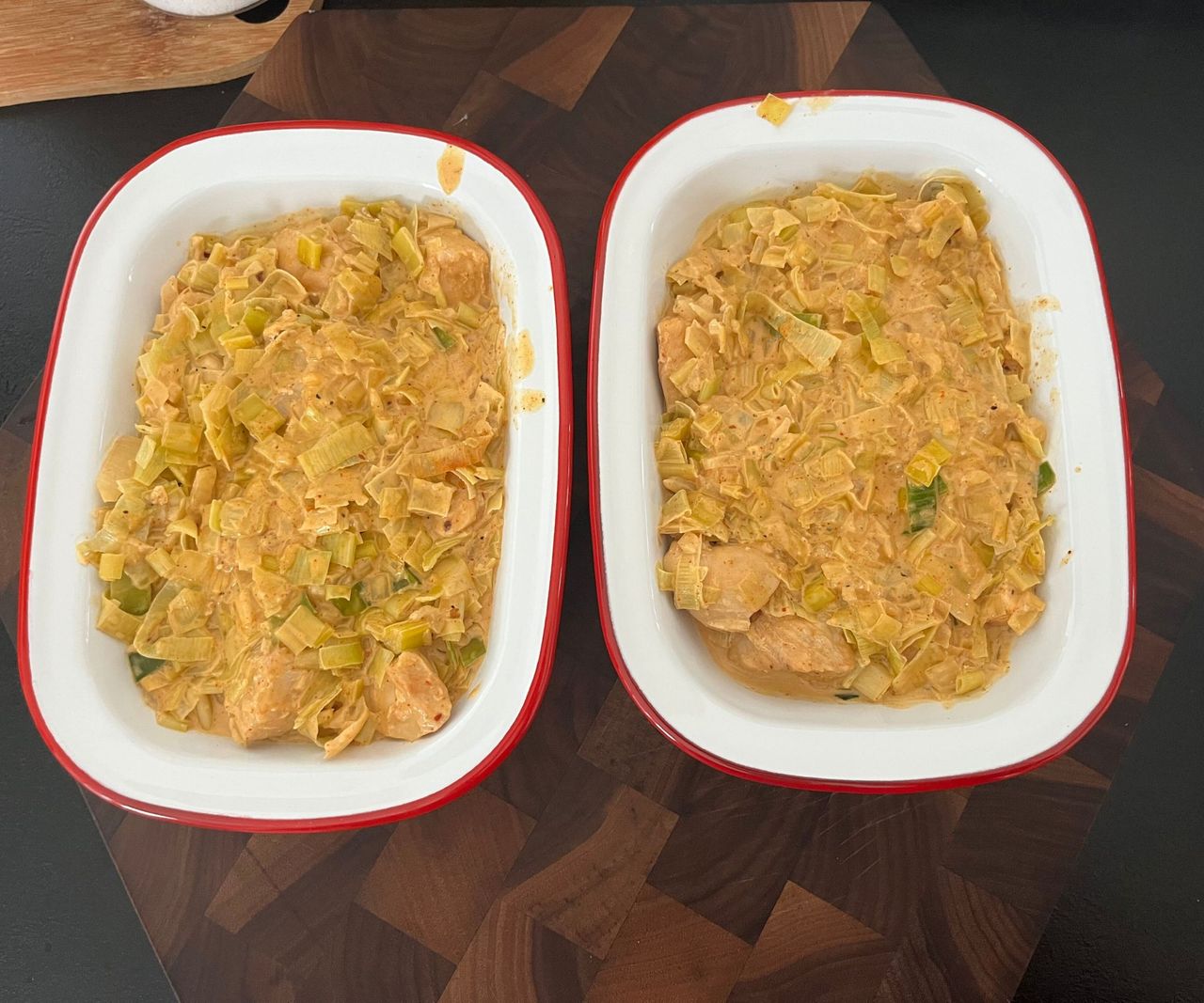 Two white enamel dishes with a red rim, with chicken pie filling inside.