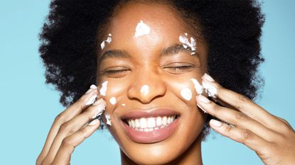 Close-up of young mixed-race woman applying white face cream face, face mask, eyes closed, with turquoise background