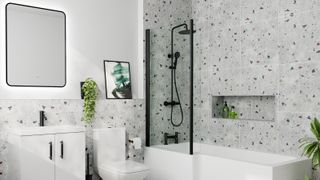 bathroom with l-shaped bath, black shower screen, toilet and white vanity unti with sink terrazzo style grey, white and black tiling on walls