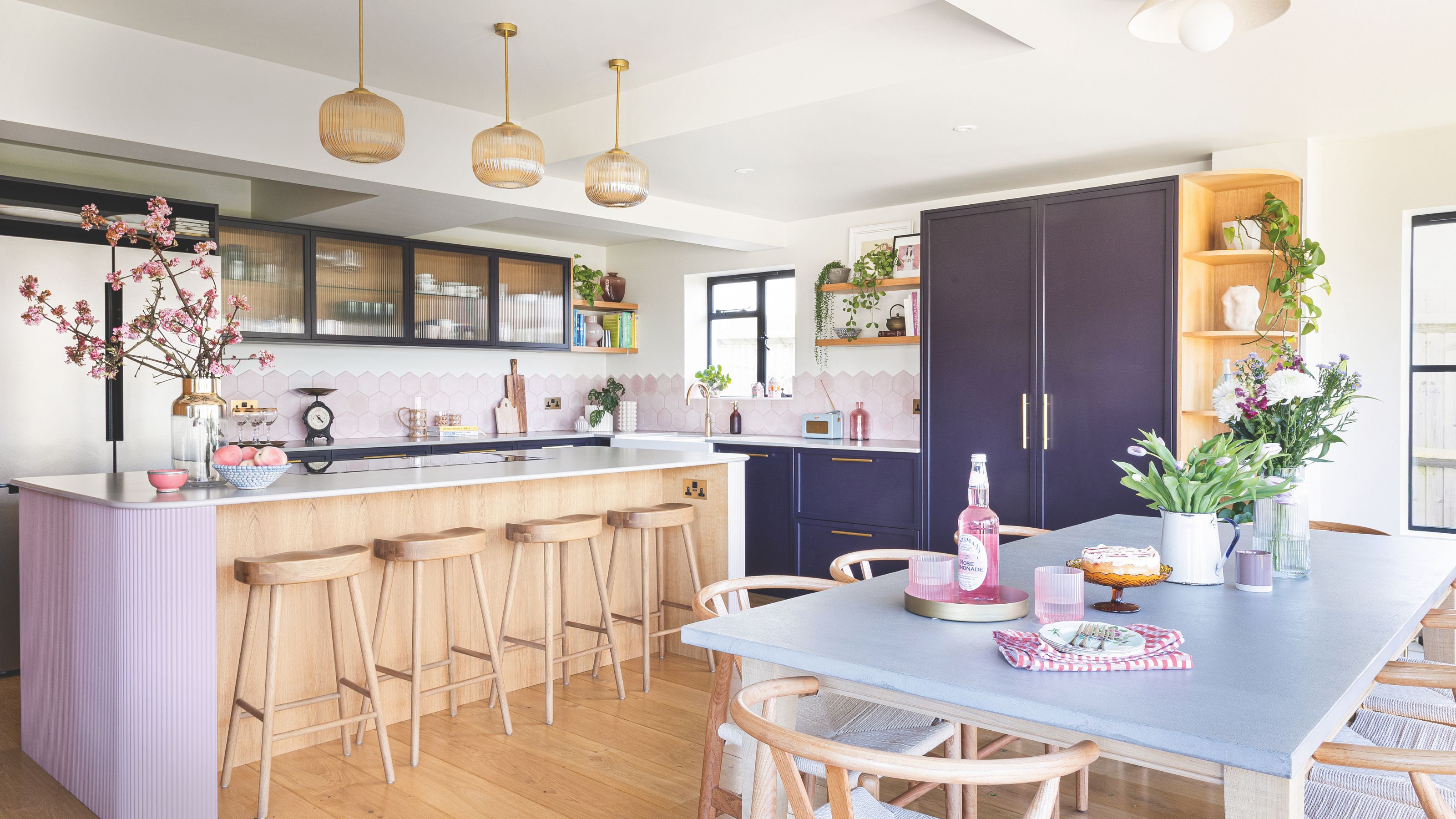 Open plan kitchen-diner with a pink, wooden kitchen island, purple cabinets, and wooden floors