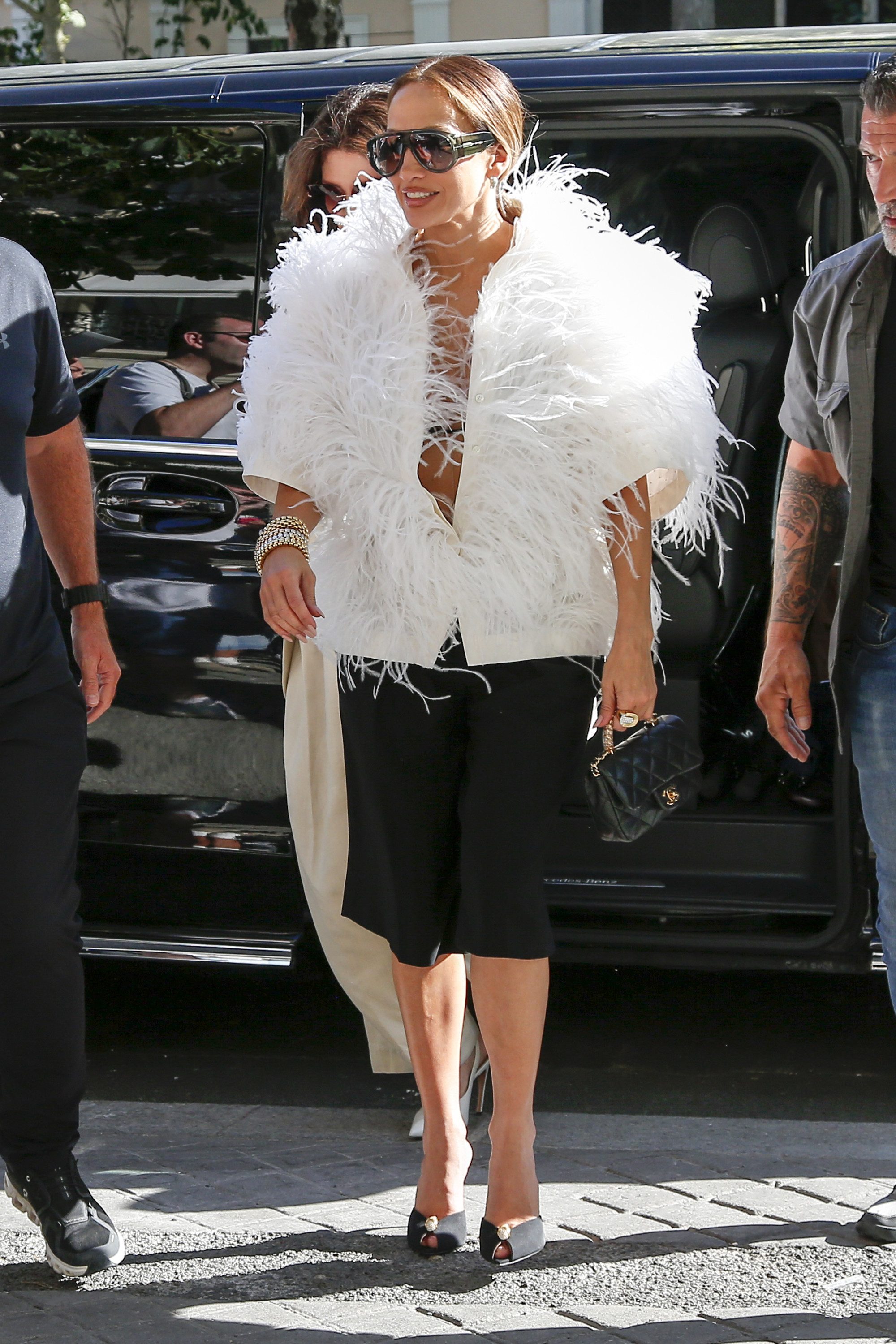 J.Lo wears a white furry top, black bermuda shorts, and black peep-toe heels.