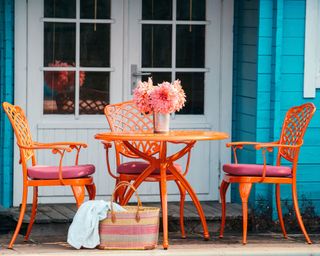A metal table and chairs painted in a bright orange outdoor paint on a blue porch