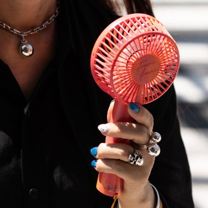 a woman carrying a portable fan with several silver rings