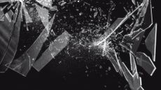 Shattered glass fragmenting into a multitude of sharp splinters pictured against a black backdrop.