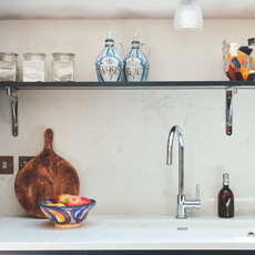 Kitchen sink with silver taps. On the side next to the sink is a wooden chopping board and fruit ball.