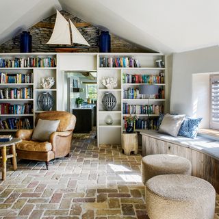 A country style cottage living room with exposed brick, bookcase and leather chair