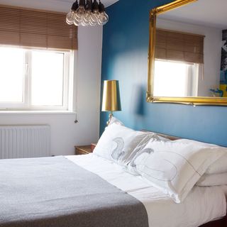 bedroom with blue feature wall and pillows on bed with mirror on wall