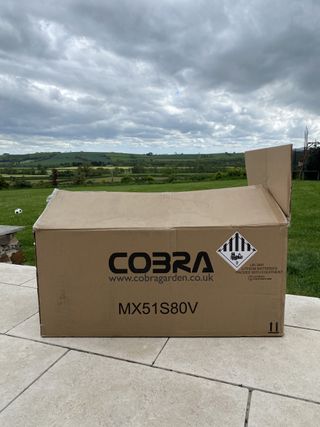 Cobra MX51S80V lawn mower in a box on a patio