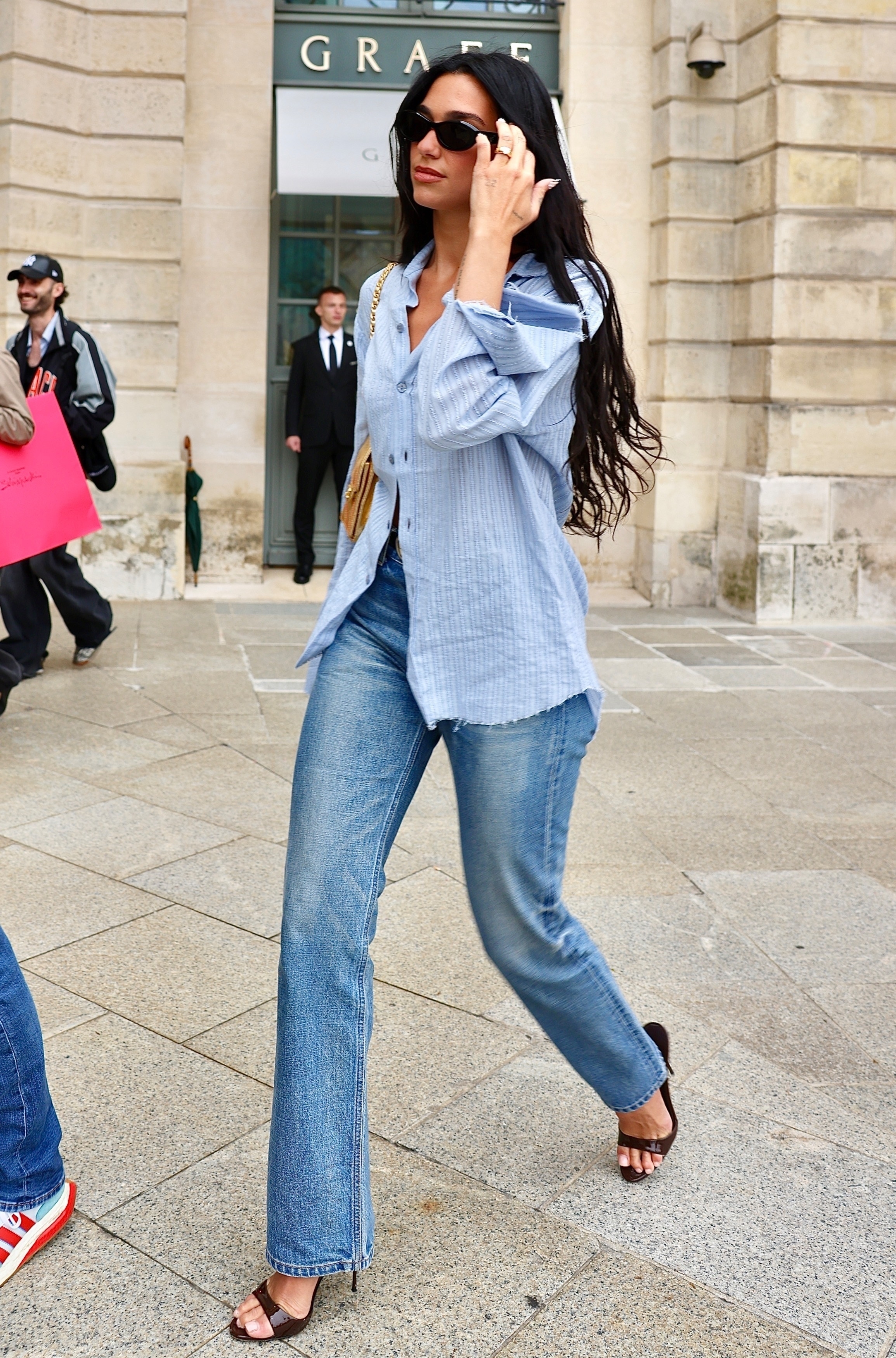 Dua Lipa wears a blue shirt, jeans and peep-toe mules as she walks down the street in Paris.