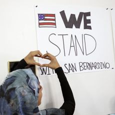 A Muslim woman raises her hands in the shape of a heart to a sign that reads "We stand with San Bernardino."