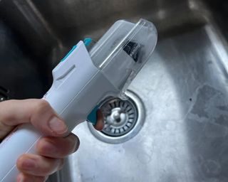 Shark StainStriker hose being cleaned with the cleaning tool, over stainless steel laundry room sink