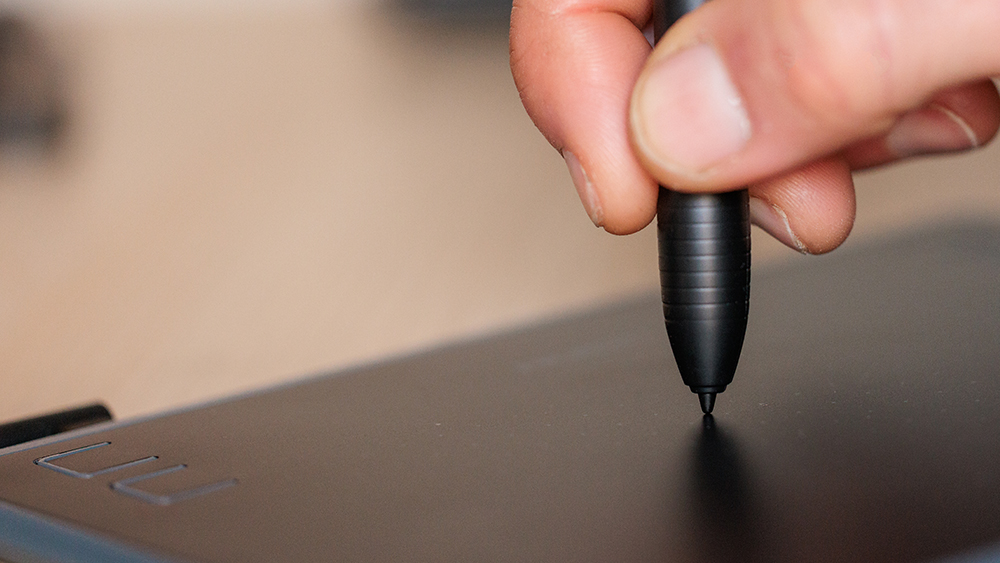 The hand and stylus of someone using a Huion H430P drawing tablet for photo editing