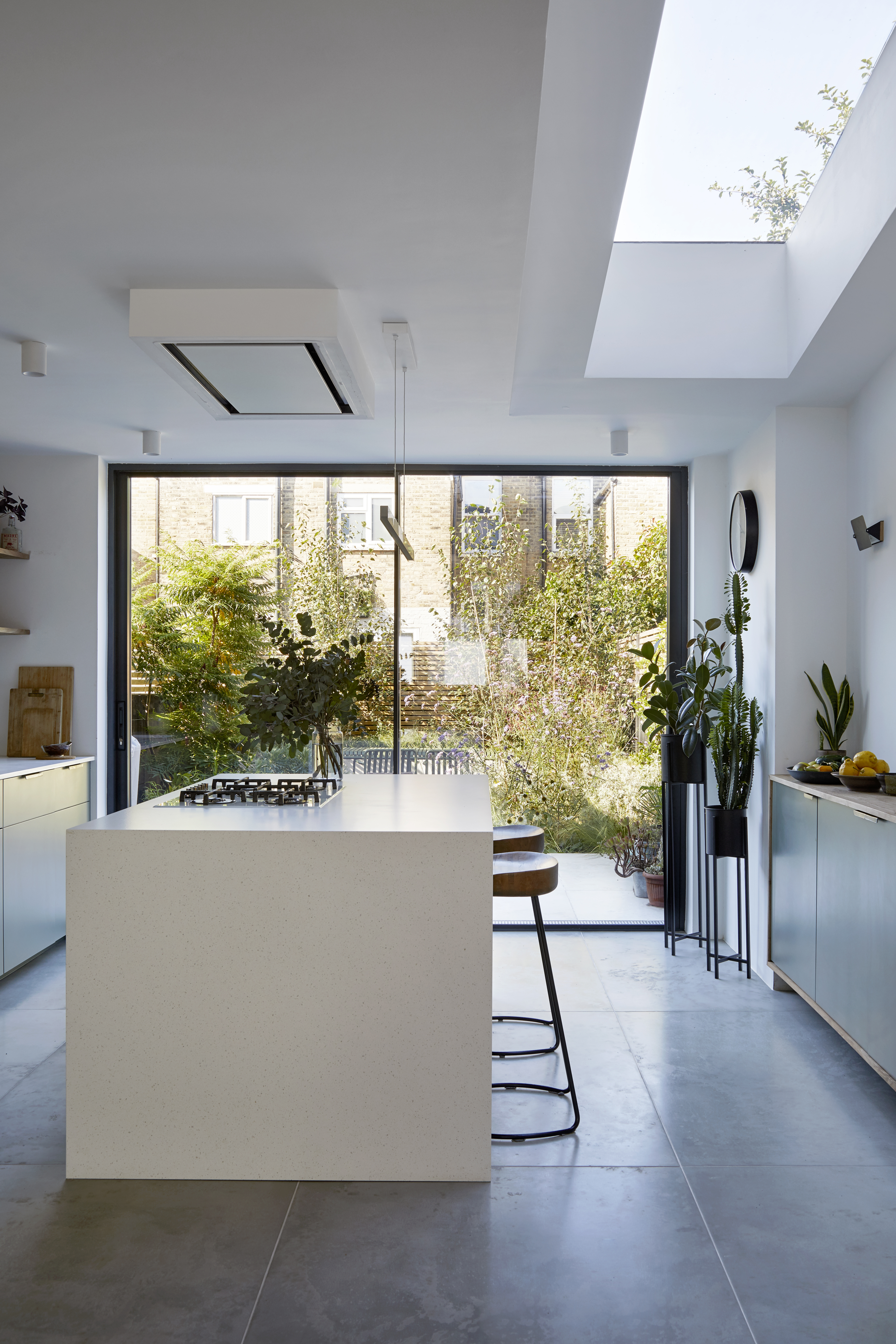 Kitchen extension with white waterfall island and bar stools. Large glass sliding doors