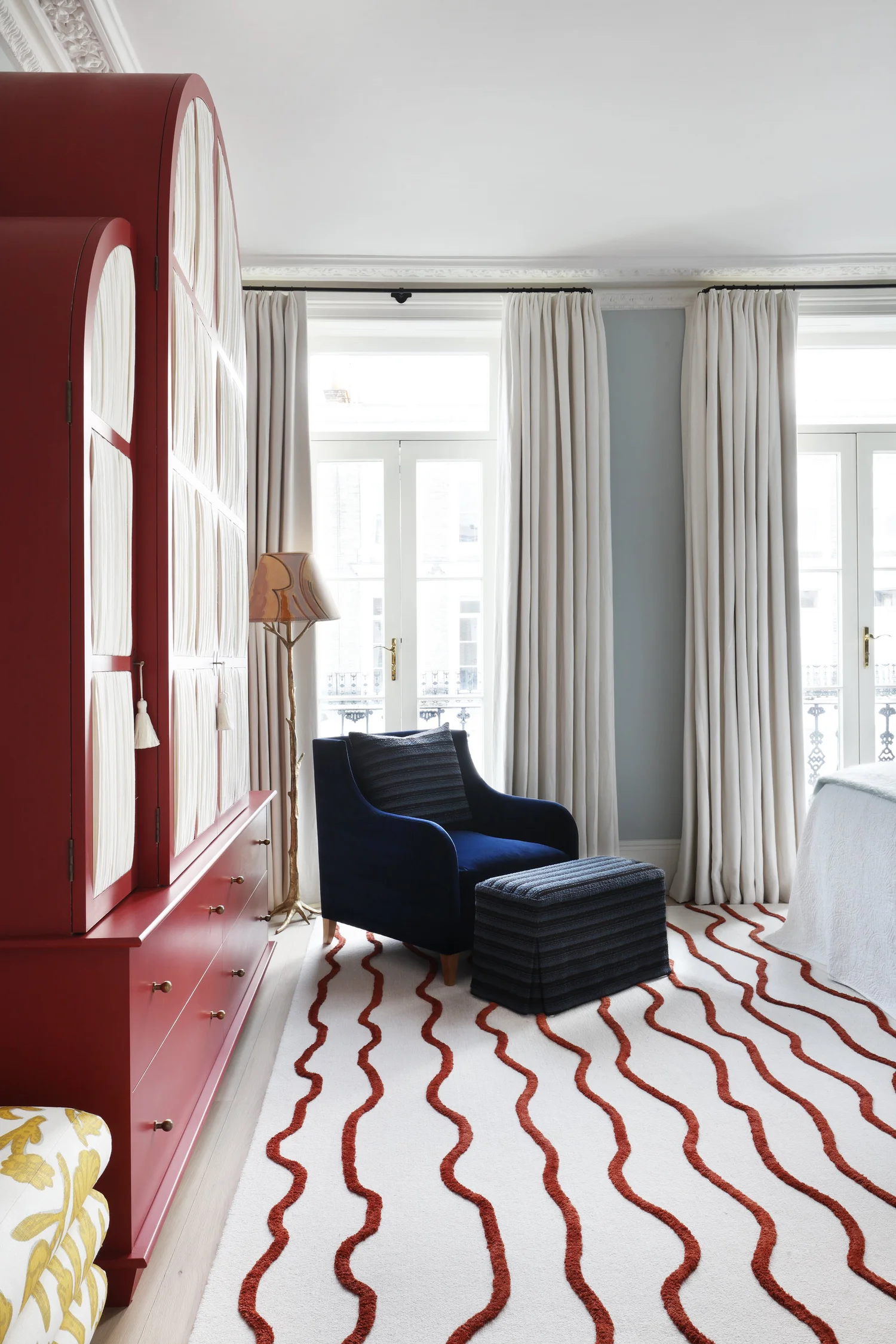Bedroom with light blue walls, white curtains and red cabinetry