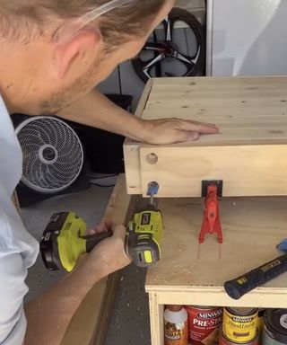 A caucasian man using electric drill to insert holes into wood for outdoor sofa DIY