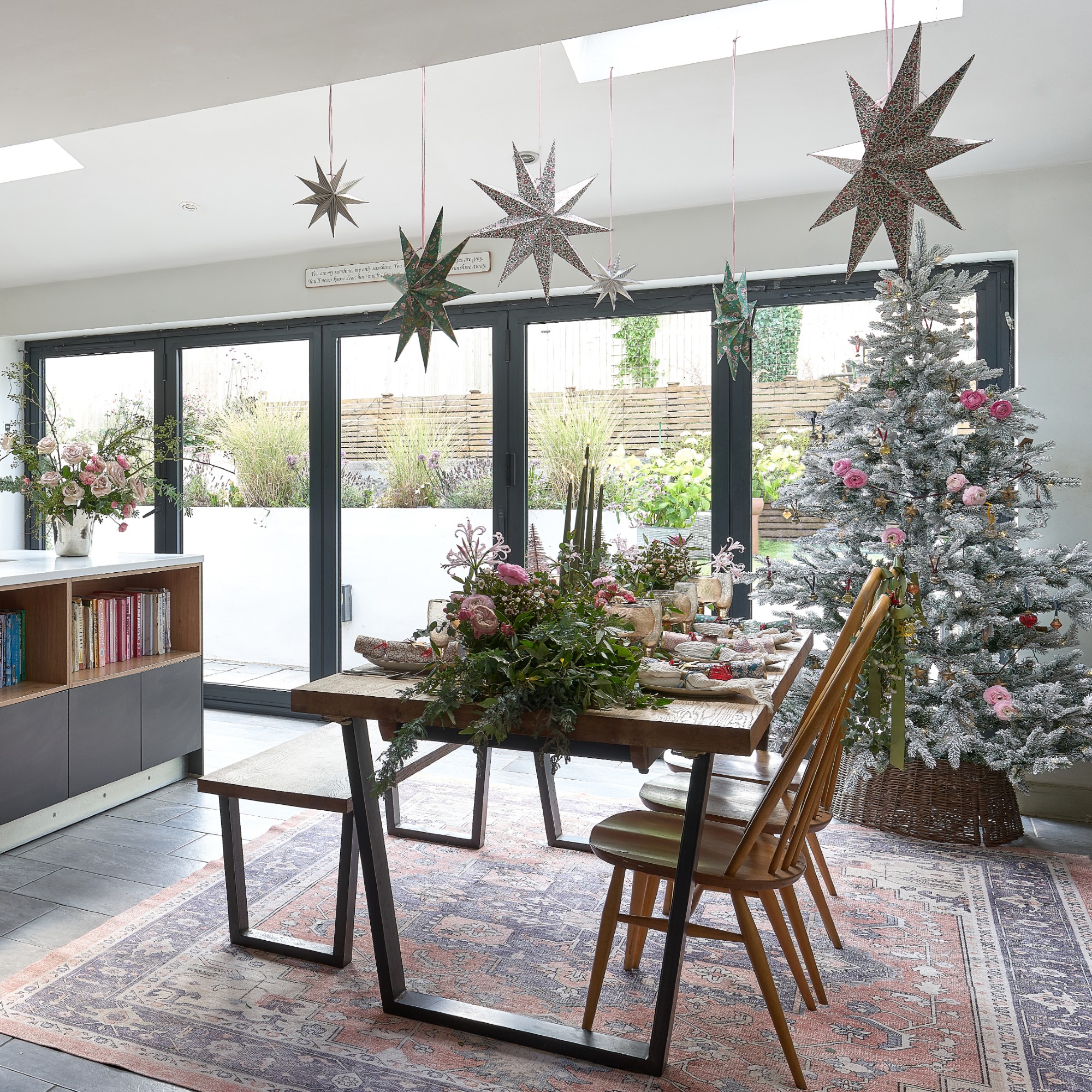 An open-plan kitchen with a dining area decorated for Christmas with a snow-covered Christmas tree in the corner