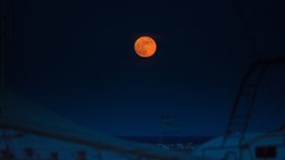 a reddish-colored moon above a seaside landscape