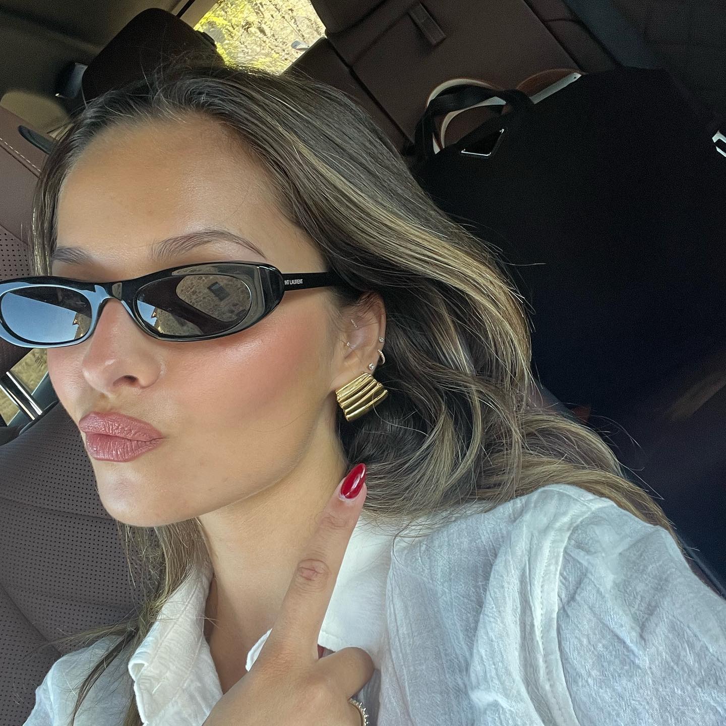 A women wearing gold earrings, black sunglasses and a white shirt