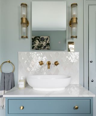 blue bathroom with white tiles, brass lights to either side of mirror and blue dresser