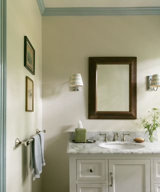 bathroom with cream walls and light blue trim detailing, marble vanity and wooden mirror