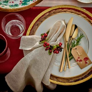 a table with red tablecloth, gold and red dining setting and a napkin tied with a mini holly wreath