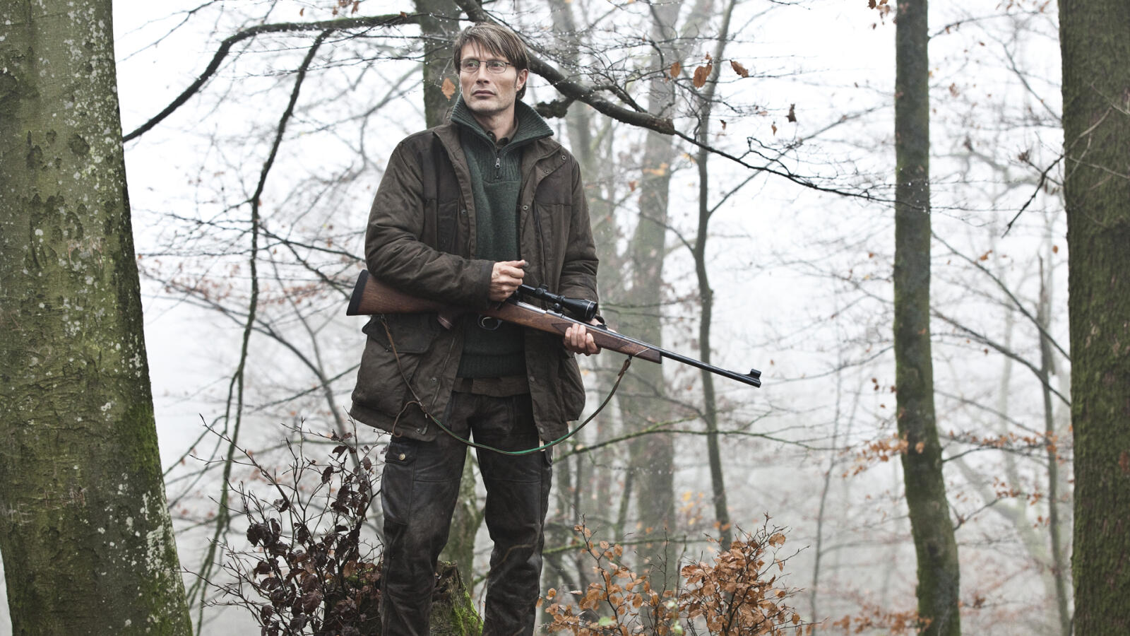Mads Mikkelsen st&amp;aring;r med ett gev&amp;auml;r i handen ute i skogen i Jakten.