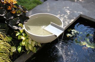 Solus Decor Water Bowl Scupper feature sitting above a pond in a paved garden