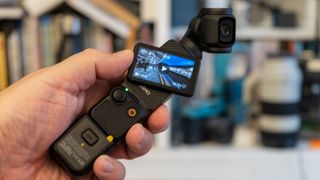 DJI OSMO Pocket 3 being held in hand in front of bookshelves