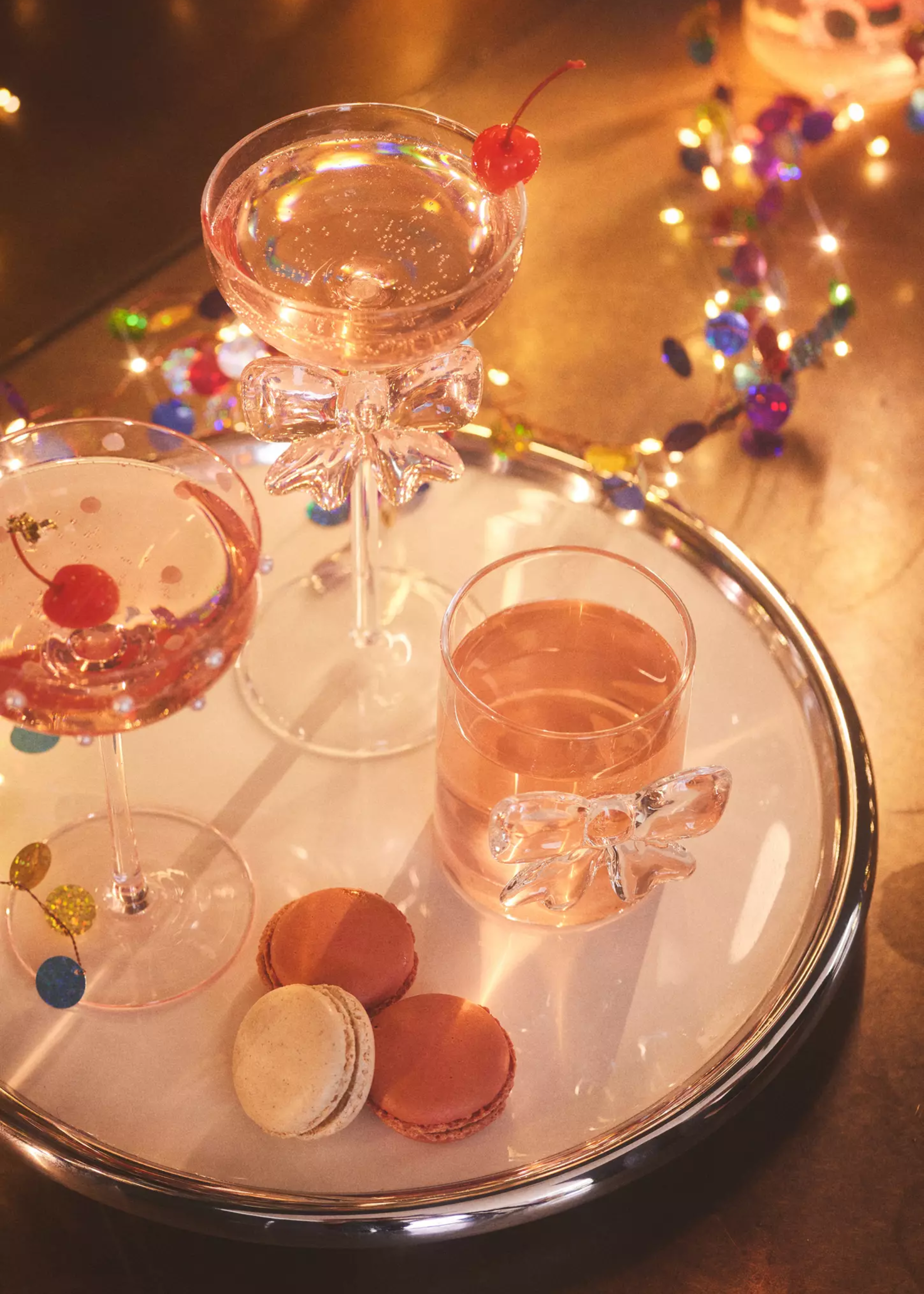 A tray with coupe glasses and cherries, featuring a glass bow detail by macaroons