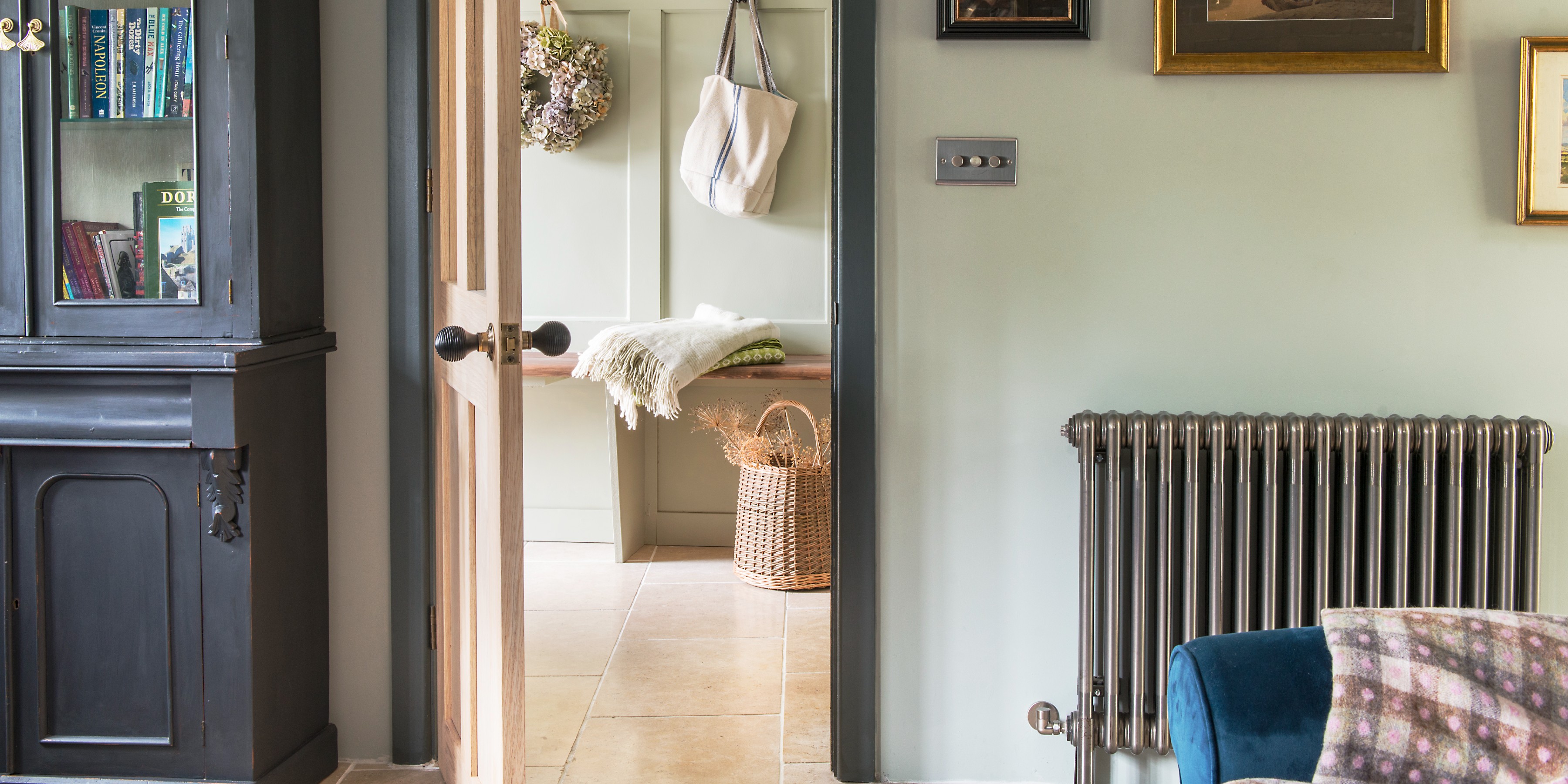 Traditional radiator on wall of pale green living room next to a doorway that leads to a hall with a bench and basket