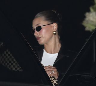 Hailey Bieber gets into a car wearing an oval diamond ring with a black jacket