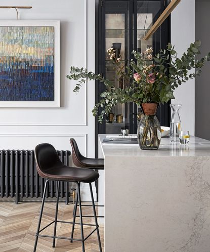 Breakfast bar ideas with a marble waterfall countertop, leather bar stools and a large vase of eucalyptus and roses. 