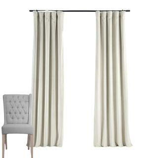 Off white velvet curtains on a black curtain rail with a grey chair with brown legs in the foreground