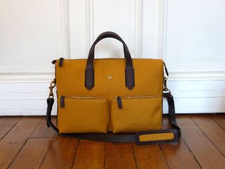A light tan coloured carry bag with dark brown centre handle and two side-facing pockets.