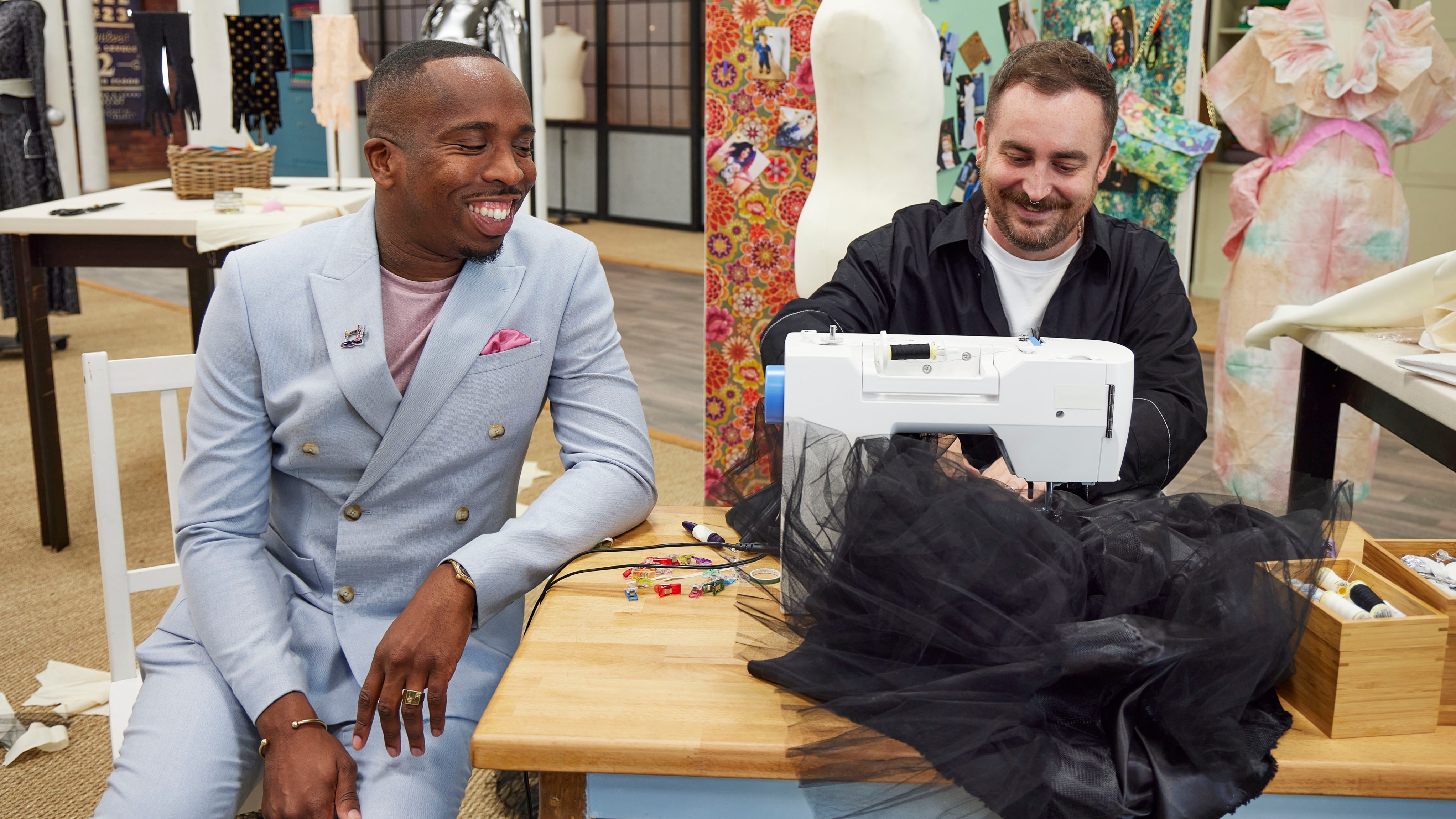 Kiell Smith-Bynoe in a light suit sitting next to winner Luke who is at a sewing machine